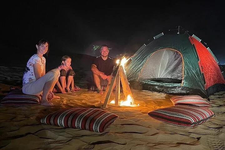 Desert safari camping in Dubai with traditional Bedouin camp set among red sand dunes at sunset