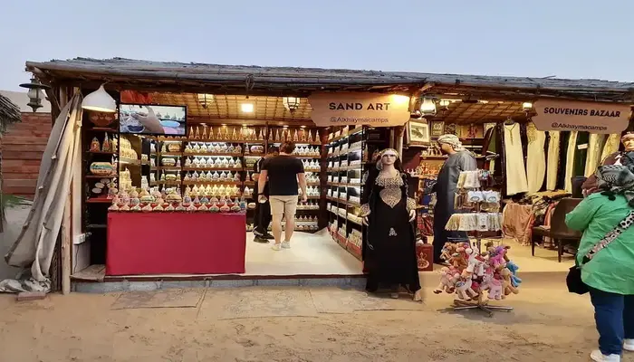 Desert safari Dubai camp shopping stalls with Bedouin handicrafts, camel souvenirs, and spices under sunset dunes