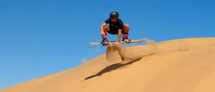 Tourist sandboarding down the red sand dunes of Lahbab Desert during Dubai desert safari at sunset
